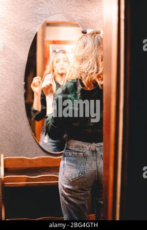 Teenager-Mädchen mit Lockenstab Blick auf sich selbst in den Spiegel zu Hause immer bereit zu gehen Stockfoto