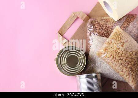Papiertüte mit Lebensmitteln Krise Nahrungsmittelvorrat für Quarantäne Isolationsperiode auf rosa Hintergrund. Reis, Buchweizen, Nudeln, Dosenfutter, Toilettenpapier Stockfoto