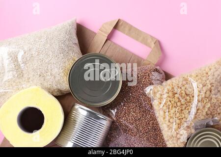 Papiertüte mit Lebensmitteln Krise Nahrungsmittelvorrat für Quarantäne Isolationsperiode auf rosa Hintergrund. Reis, Buchweizen, Nudeln, Dosenfutter, Toilettenpapier Stockfoto