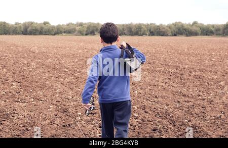 Boy geht durch das Feld und trägt seine Drohne mit ihm, um es zu blasen Stockfoto
