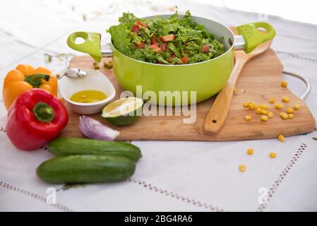 Oliven auf einer kleinen weißen Schüssel . Rote und orangefarbene Paprika. In Scheiben geschnittene grüne Zitrone. Holzlöffel. Gurken. Maiskörner . Pfeffer und Salat Salat Salat in einem grünen Stockfoto