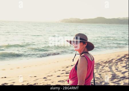 Ältere Frau in Strohhut am Strand bei Sonnenuntergang Stockfoto
