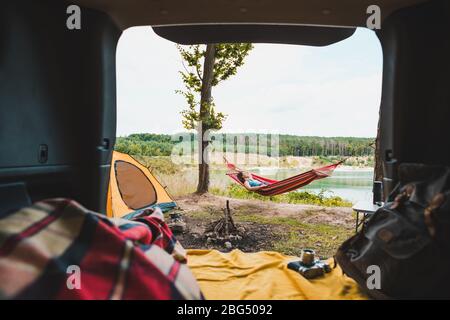 Ein Paar mit Blick auf die Person, das auf einer Camping-Frau ruht und in Hängematte mit wunderschönem Blick auf den Waldsee liegt Stockfoto