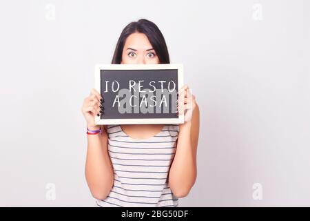 Schöne junge Frau hält und zeigt 'io resto a casa' auf einer Tafel. Copyspace. Coronavirus und Quarantäne Konzept. Italienische Sprache. Stockfoto