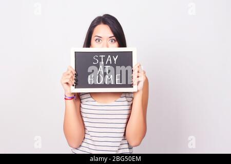 Schöne junge Frau, die "Zuhause" hält und auf einer Tafel zeigt. Copyspace. Coronavirus und Quarantäne Konzept. Stockfoto