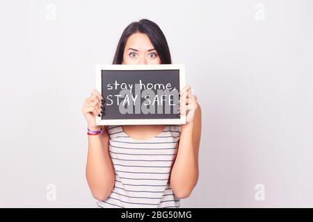 Schöne junge Frau hält und zeigt "Bleib nach Hause, bleib sicher" auf einer Tafel. Copyspace. Coronavirus und Quarantäne Konzept. Stockfoto