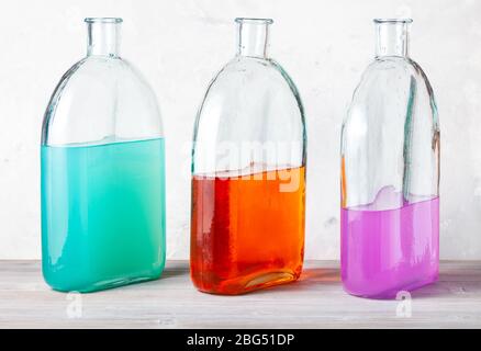 Drei Flaschen mit farblichen Aquarelllösungen auf grauer Holzplatte in der Nähe von grauer Betonwand Stockfoto