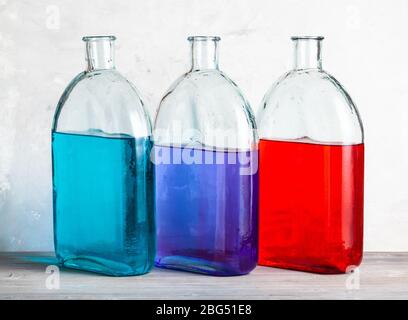 Drei Flaschen mit Farbtintenlösungen auf grauer Holzplatte in der Nähe von grauer Betonwand Stockfoto