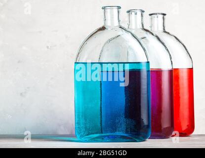 Glasflaschen mit Farbtintenlösungen auf grauer Holzplatte in der Nähe von grauer Betonwand Stockfoto