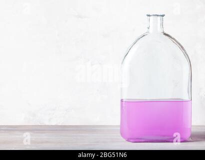 Glasflasche mit rosa Aquarelllösung auf grauem Holzbrett in der Nähe von grauer Betonwand Stockfoto