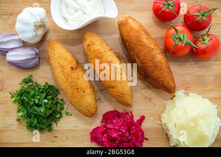 Ukrainische Tradition Essen auf einem Holzbrett. Rotkohl Sauerkraut in einer kleinen Schüssel . Kartoffelpüree . Mayonnaise, Knoblauch, Zwiebeln, Tomaten. Gehackt Stockfoto