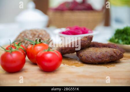 Fleischschnitzel, gebackener Buchweizen auf einem Holzbrett. Rotkohl-Sauerkraut . Knoblauch, Zwiebeln, Tomaten. Gehackter Koriander. Hausgemachte Koteletts mit Haferflocken Stockfoto