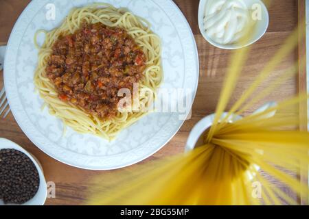 Spaghetti Bolognese mit Hackfleisch, Zwiebel, gehackte Tomaten, Tomatenmark . Rohe Spaghetti-Pasta in einer Schüssel. Schwarzer Pfeffer, Mayonnaise in einer Schüssel Stockfoto