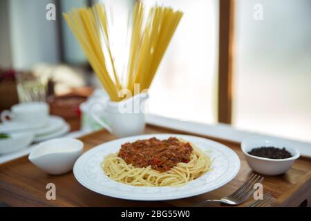 Spaghetti Bolognese mit Hackfleisch, Zwiebel, gehackte Tomaten, Tomatenmark . Rohe Spaghetti-Pasta in einer Schüssel. Schwarzer Pfeffer, Mayonnaise in einer Schüssel Stockfoto