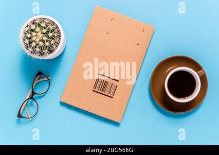 Flaches Lay mit Box-Paket zum Senden, Kaffeetasse, Brillen und Kaktus auf blauem Hintergrund. Senden oder Empfangen von Waren. Versand- und Lieferkonzept Stockfoto