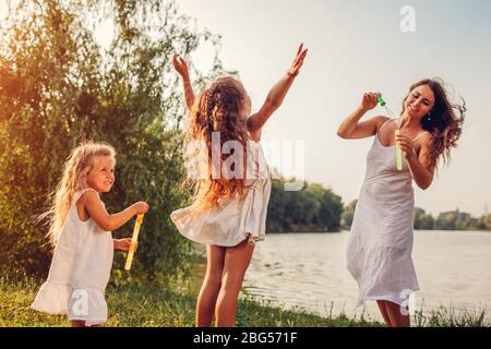 Muttertag. Mutter hilft Töchtern, Blasen im Frühlingspark zu blasen. Kinder, die Spaß beim Spielen und Bläschen fangen Stockfoto