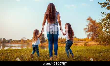 Familienspaziergang am Sommerfluss bei Sonnenuntergang. Mutter und ihre Töchter haben Spaß im Freien. Stockfoto
