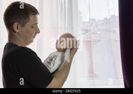 Ein junger Mann hält sanft ein Baby in seinen Armen. Das kleine Mädchen ist frech. Krampf Stockfoto