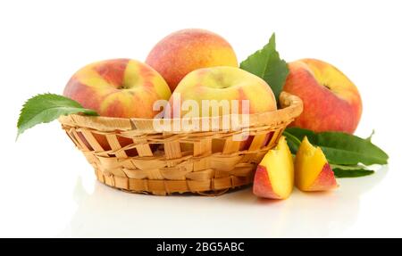 Reife süße Pfirsiche mit Blättern im Korb, isoliert auf weiß Stockfoto