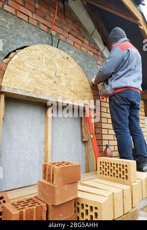 Der Meister in einem blauen Overall baut eine Wand aus Backstein.2020 Stockfoto