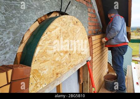 Der Meister in einem blauen Overall baut eine Wand aus Backstein.2020 Stockfoto