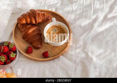 Frühstück im Bett, Tablett mit Tasse Kaffee, frische Croissants und Erdbeeren Stockfoto