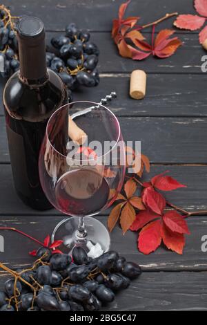 Flasche Wein, Glas, Trauben und Blätter auf schwarzem Holzhintergrund. Stockfoto