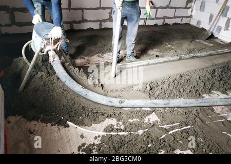 Der Arbeiter führt einen Sand-Zement-Bodentrich über der Fußbodenheizung durch.2020 Stockfoto