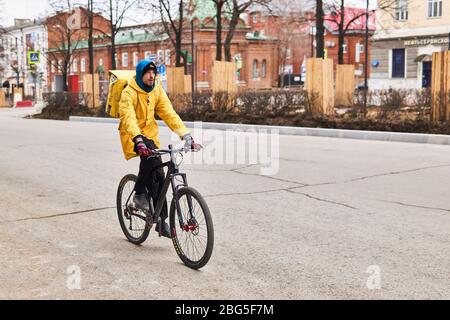 Perm, Russland - 19. April 2020: Kurier-Online-Lebensmittelzustelldienst fährt ein Fahrrad auf einer leeren Straße während einer Coronavirus-Pandemie Stockfoto