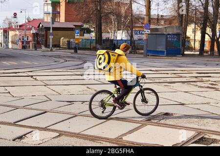 Perm, Russland - 19. April 2020: Kurier Online-Lebensmittelzustellung fährt ein Fahrrad auf einer leeren Straße während der Quarantäne in Verbindung mit dem epidem Stockfoto