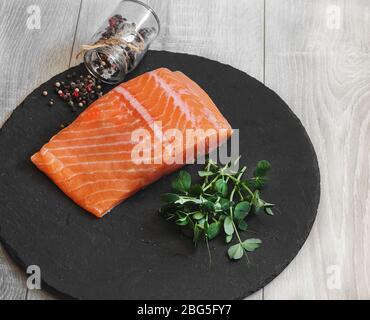 Ein Stück rohes Lachsfischfilet, Gewürze und Erbsensprossen liegen auf einer Steinoberfläche Stockfoto