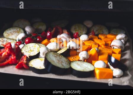 Gesundes Detox-Abendessen aus verschiedenen Gemüsesorten wie Aubergine, roter Pfeffer, Kirschtomaten, Butternusskürbis, Pilze. Scheiben rohes Gemüse, das für das Braten vorbereitet wird, einfache Familienmahlzeit Stockfoto