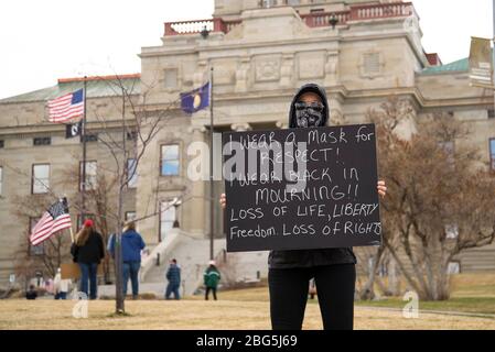 Helena, Montana - 19. April 2020: Eine Protestierende trägt ganz schwarz mit einer Bandana-Maske und hält ein Zeichen über Verlust von Leben, Freiheit und Freiheit. Bei t Stockfoto