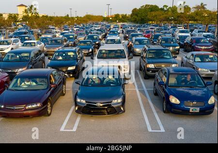 West Palm Beach, Florida, USA. April 2020. Die Autos stehen in einem Drive-up-Lebensmittelverteilungszentrum auf dem Parkplatz der Palm Beach Outlets. Die Menschen erhalten eine Woche Versorgung mit Eiweiß, frischen Produkten, Eiern, Milch und anderen wichtigen Gütern. Die Spenden sind auf 800 Autos auf einer First come first serve Basis jeden Montag begrenzt. Palm Beach Outlets hat sich mit der Ernährung von Süd-Florida zusammengetan, um denjenigen zu helfen, die während der Coronavirus-Pandemie kämpfen. Kredit: Gregg Lovett/ZUMA Wire/Alamy Live News Stockfoto