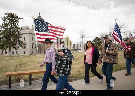 Helena, Montana - 19. April 2020: Gruppe von Demonstranten, die amerikanische Fahnen halten, Mann, der auf die Kamera zeigt. Demonstranten bei einem Protest gegen GO Stockfoto