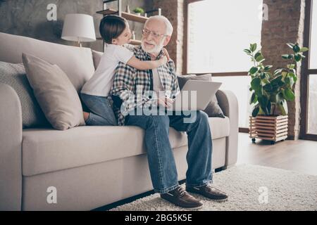 Profil Foto von lustigen alten Großvater kleine Enkelin sitzen Sofa umarmen Aufenthalt Haus Quarantäne Sicherheit Film ansehen Notebook sprechen skype moderne Einrichtung Stockfoto