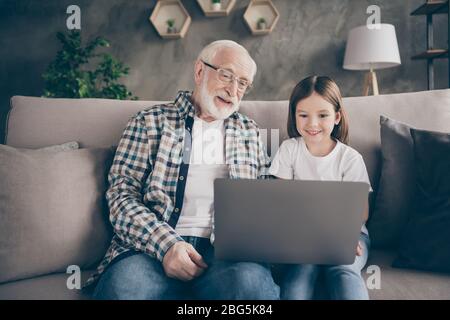 Foto von lustigen zwei Personen alt Großvater kleine Enkelin sitzen Sofa bleiben Haus Quarantäne Sicherheit Film ansehen Notebook sprechen skype modernes Design Stockfoto