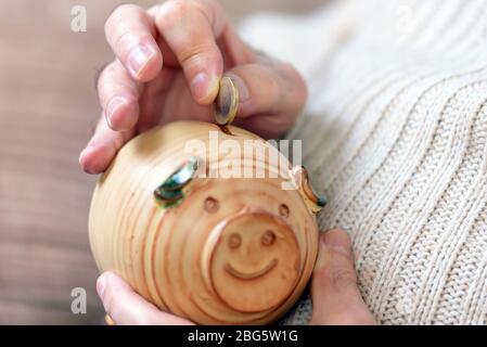 Sparungen, Geld, Rentenversicherung, Ruhestand und Menschen Konzept - Nahaufnahme von älteren Mann Hand setzen Münze in Sparschwein . Stockfoto