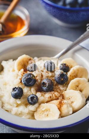 Schließen Sie das Uo von Milchreis-Haferbrei mit Blaubeere, Banane, Honig und Zimt, cremigem Reis-Pudding oder französischem Riz au LAIT in einer Metallschale Stockfoto