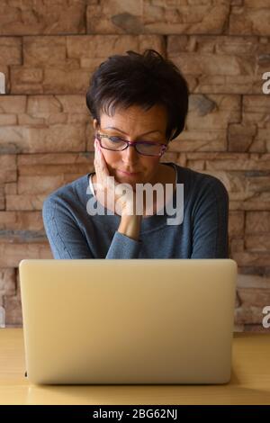 Reife schöne Frau mit Laptop, während das Tragen von Brillen und ruht Kinn auf der Hand Stockfoto