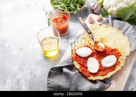 Hausgemachte glutenfreie Cauliflower Pizza Kruste Teig mit Tomaten Marinara-Sauce, Mozzarella-Käse und Rucola auf grauem Hintergrund.Gemüsealternative Stockfoto