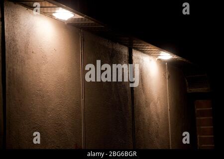 Zwei große Topflichter beleuchten eine Betonwand im Dunkeln. Beleuchtete leere Gebäudewand in der Nacht. Stockfoto