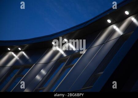 Helle Topflichter beleuchten einen Beton eine moderne Gebäudefassade in der Dämmerung. Moderne Architektur in weiß zur blauen Stunde beleuchtet. Stockfoto