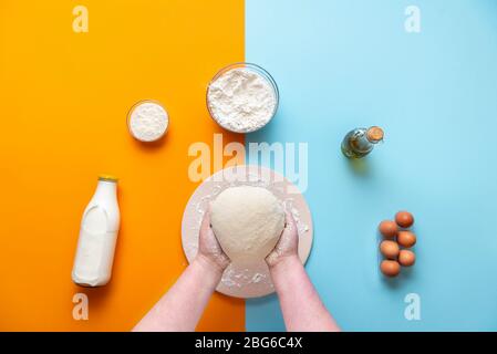 Brot zu Hause mit Bio-Mehl und Sauerteig backen. Teig über der Ansicht kneten. Backzutaten auf einem bunten Küchentisch. Stockfoto