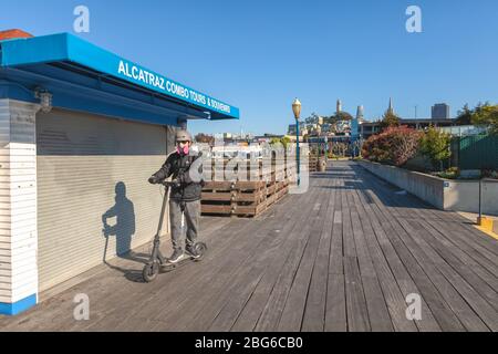 Mann mit Maske und Schutzkleidung fährt auf dem Roller am Pier 39 während der Stadtsperrung wegen COVID-19 Pandemie, San Francisco, Kalifornien, USA. Stockfoto