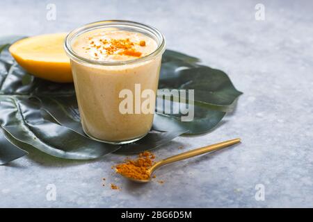Gelber Mangojoghurt oder Smoothie auf grauem Hintergrund. Kurkuma Lassie oder Lassi in Glas. Stockfoto
