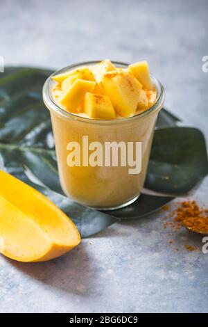 Gelber Mangojoghurt oder Smoothie auf grauem Hintergrund. Kurkuma Lassie oder Lassi in Glas. Stockfoto