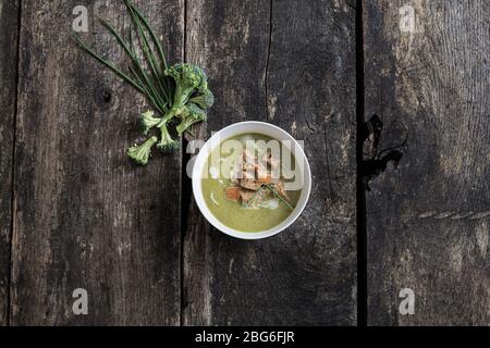 Draufsicht der köstlichen cremigen Brokkoli-Suppe mit hausgemachten Croutons Brot und Hafercreme. Auf rustikalem Holzschreibtisch mit Brokkoli und Schnittlauch an der Seite. Stockfoto