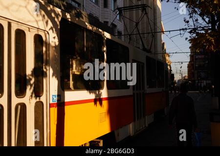 Alte orangefarbene Straßenbahn an der Haltestelle in der europäischen Hauptstadt in der zentralen Innenstadt Straße. Perspektivische Foto mit Bäumen und unscharfen Hintergrund in Licht und Schatten CO Stockfoto