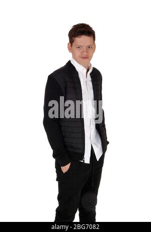 Ein junger Teenager, der in einer schwarzen Jacke und Hose im Studio steht, mit den Händen in der Tasche, isoliert auf weißem Hintergrund Stockfoto